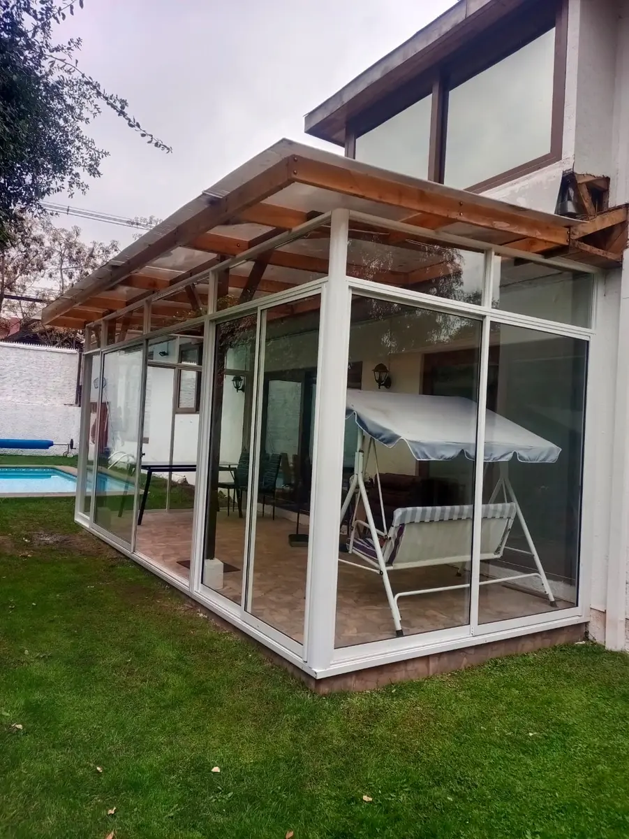 Cierre de quincho con paneles de vidrio y perfiles de aluminio blanco junto a una piscina