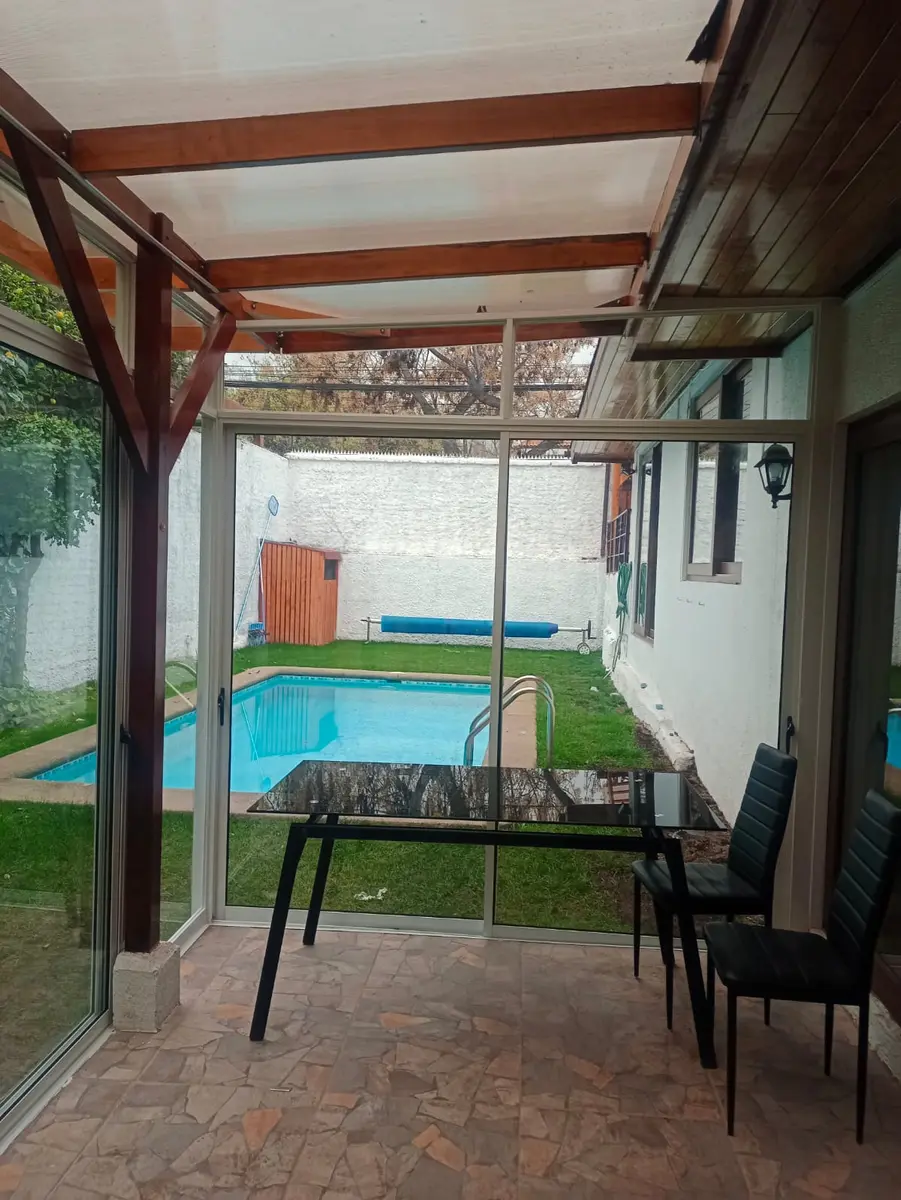 Vista desde el interior de una terraza cerrada con vidrio hacia el jardín y la piscina