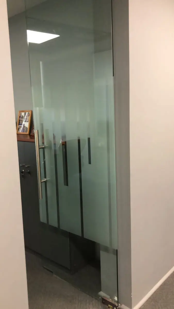 Puerta de vidrio templado con tirador vertical en una oficina