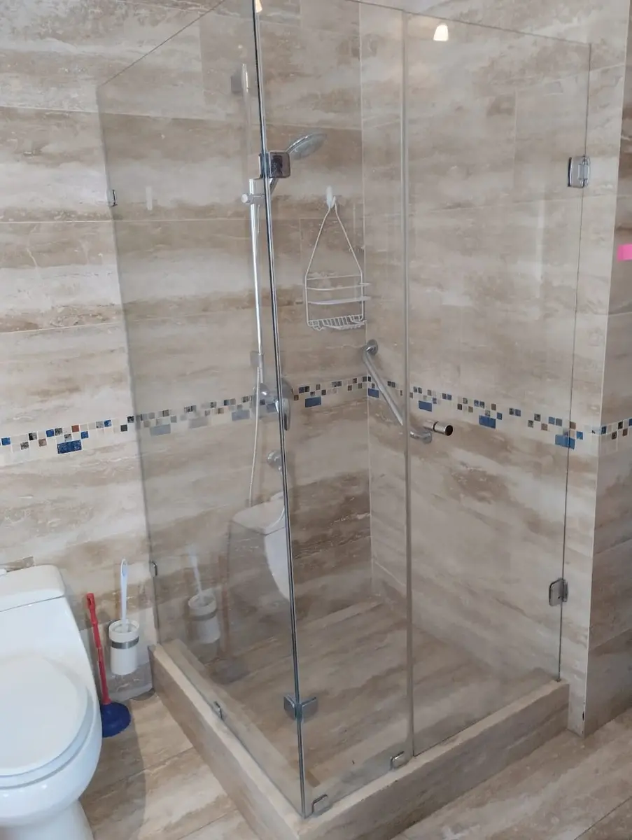Shower door de vidrio en esquina con herrajes cromados en un baño con porcelanato
